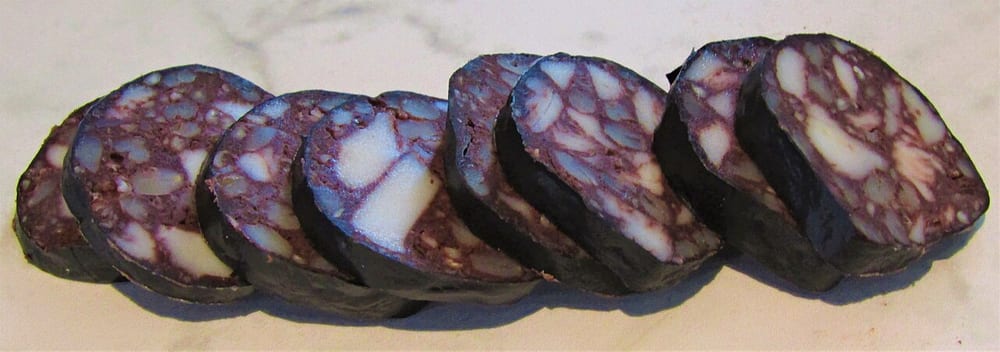 Sliced black pudding showing distinct white cubes of fat set in a dark, crumbly grain matrix