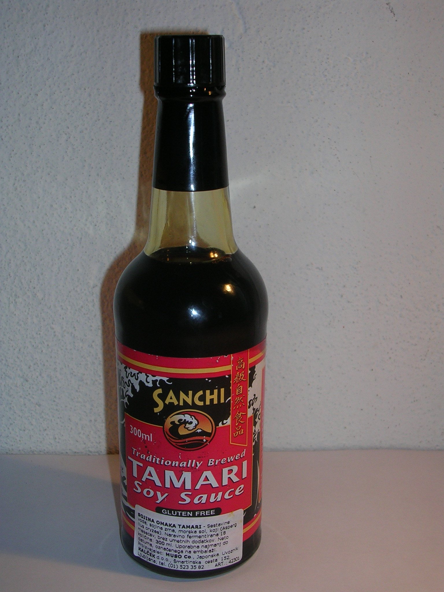 A bottle of traditionally brewed tamari, dark and heavy in the glass, its label carrying a gluten-free claim