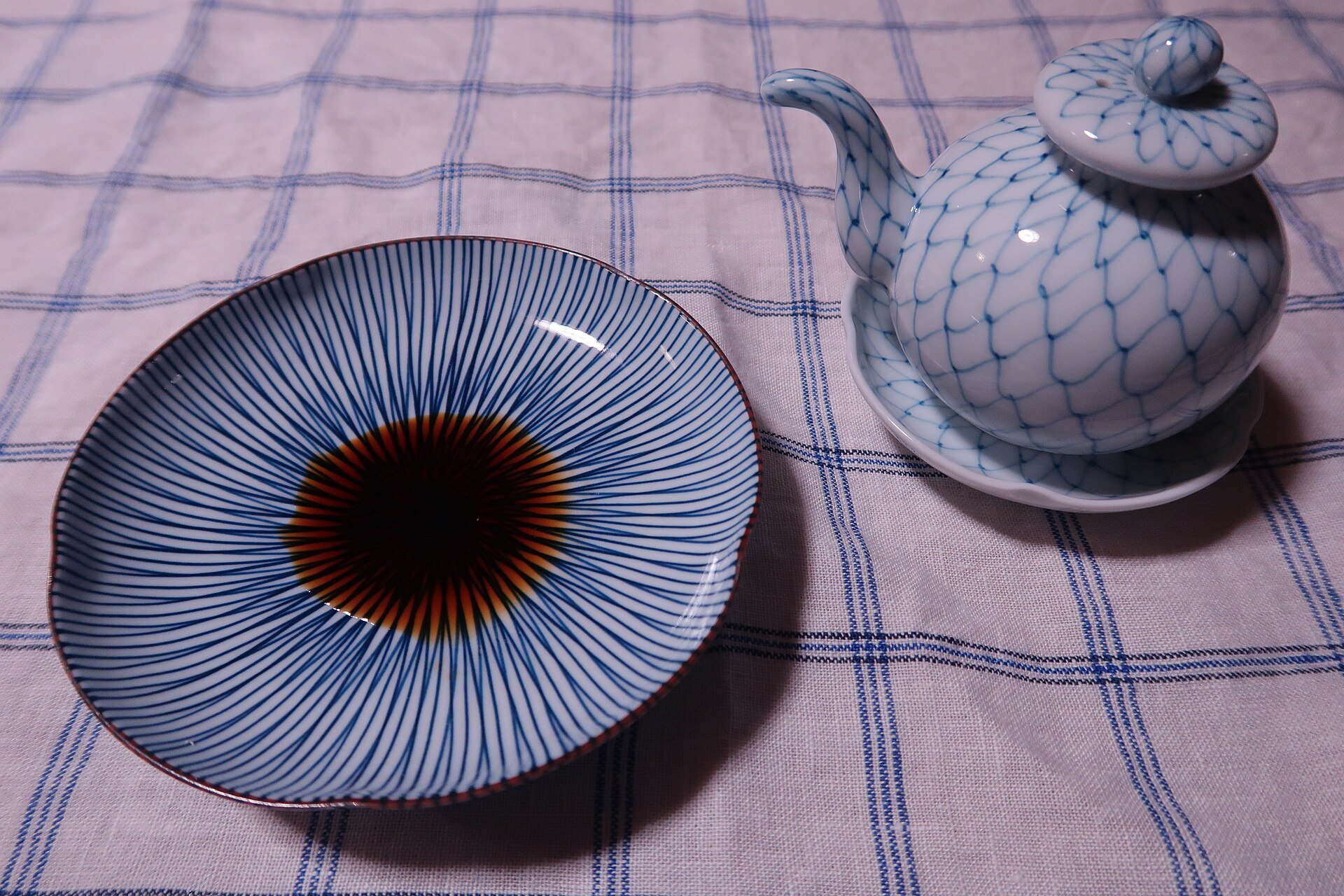A ceramic shoyu-sashi cruet beside a small dipping plate on a checked cloth