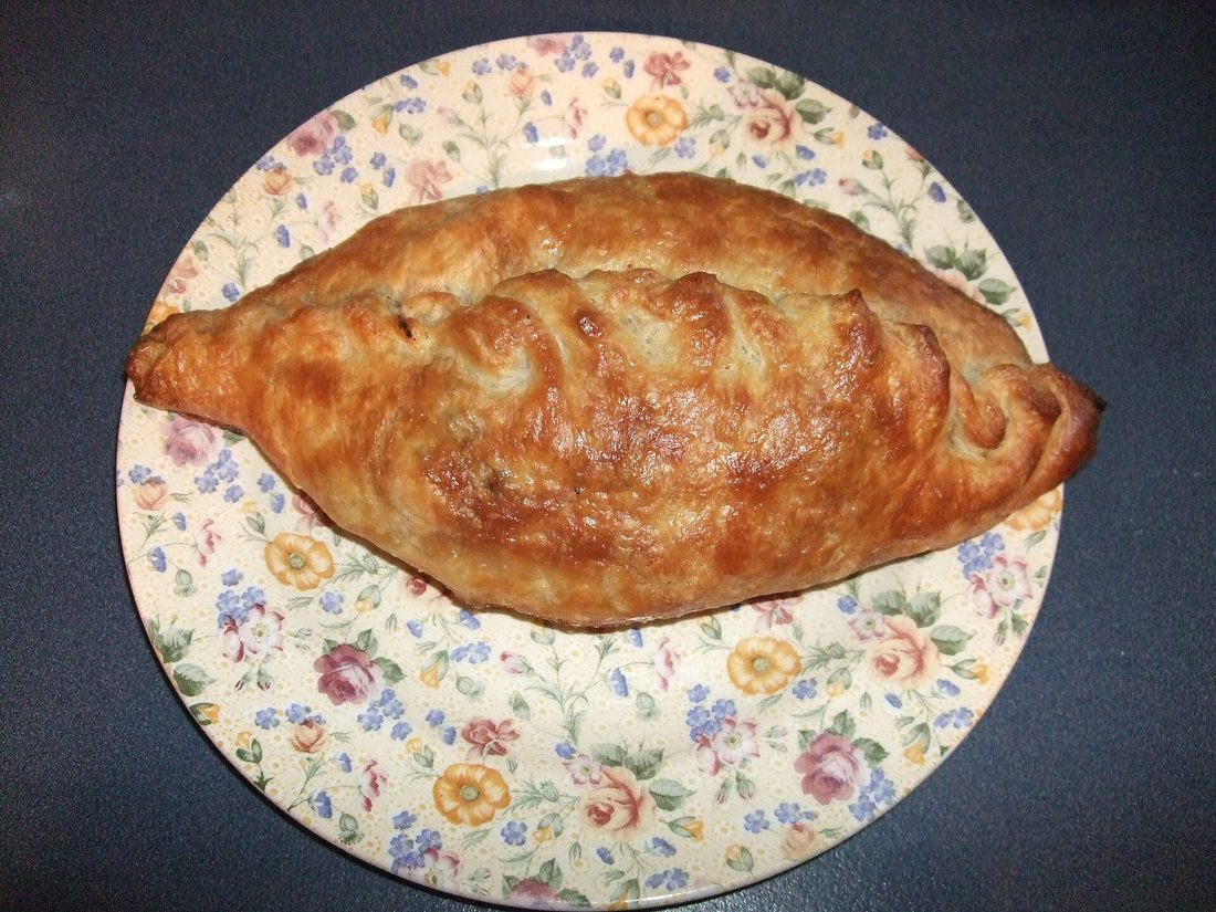 A golden D-shaped pasty on a paper plate with a thick crimped edge
