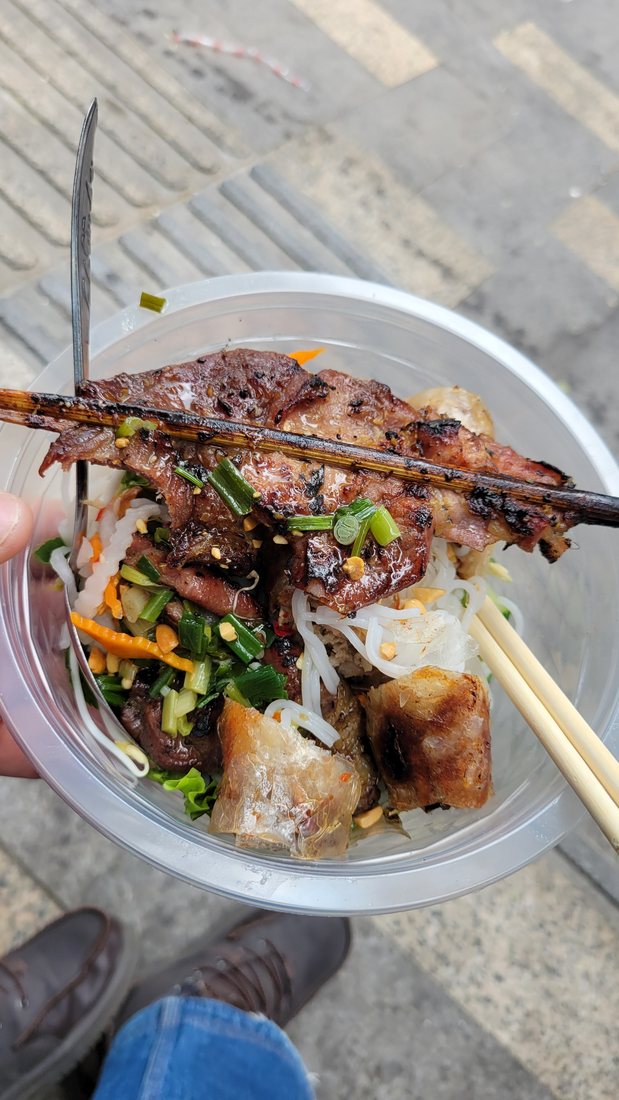 The bowl I walked away with — vermicelli underneath, grilled pork off the skewer, a fried spring roll, pickled carrot and daikon, herbs, crushed peanuts