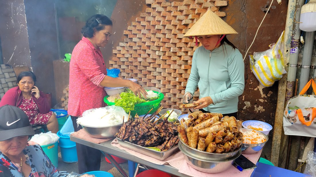 The stall: the charcoal grill going, trays of grilled pork and fried rolls laid out, tubs of herbs and pickle within reach
