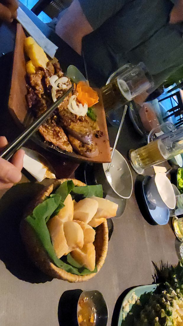 Grilled meat on a wooden board, with a basket of crackers and a pot of something green alongside