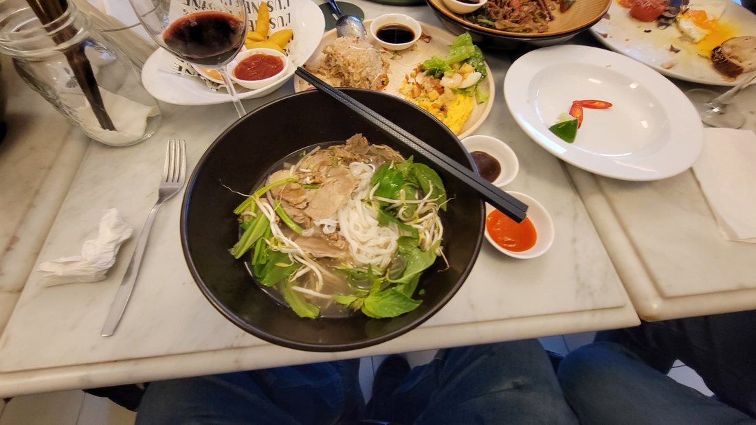 The other phở: a black bowl on a marble table with a knife and fork beside it, a bean-sprout and herb plate, a saucer of chilli sauce — 18 March, ten to six in the evening
