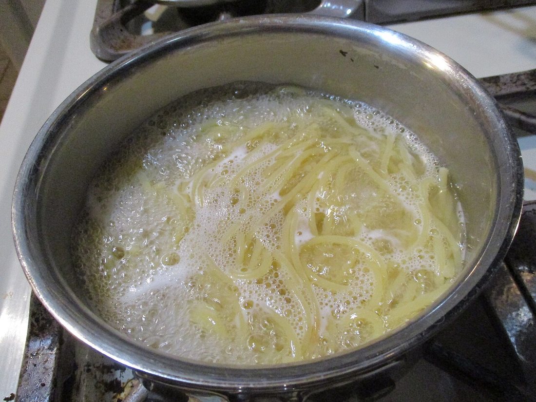 Spaghetti boiling in a stainless steel pot on a gas stove