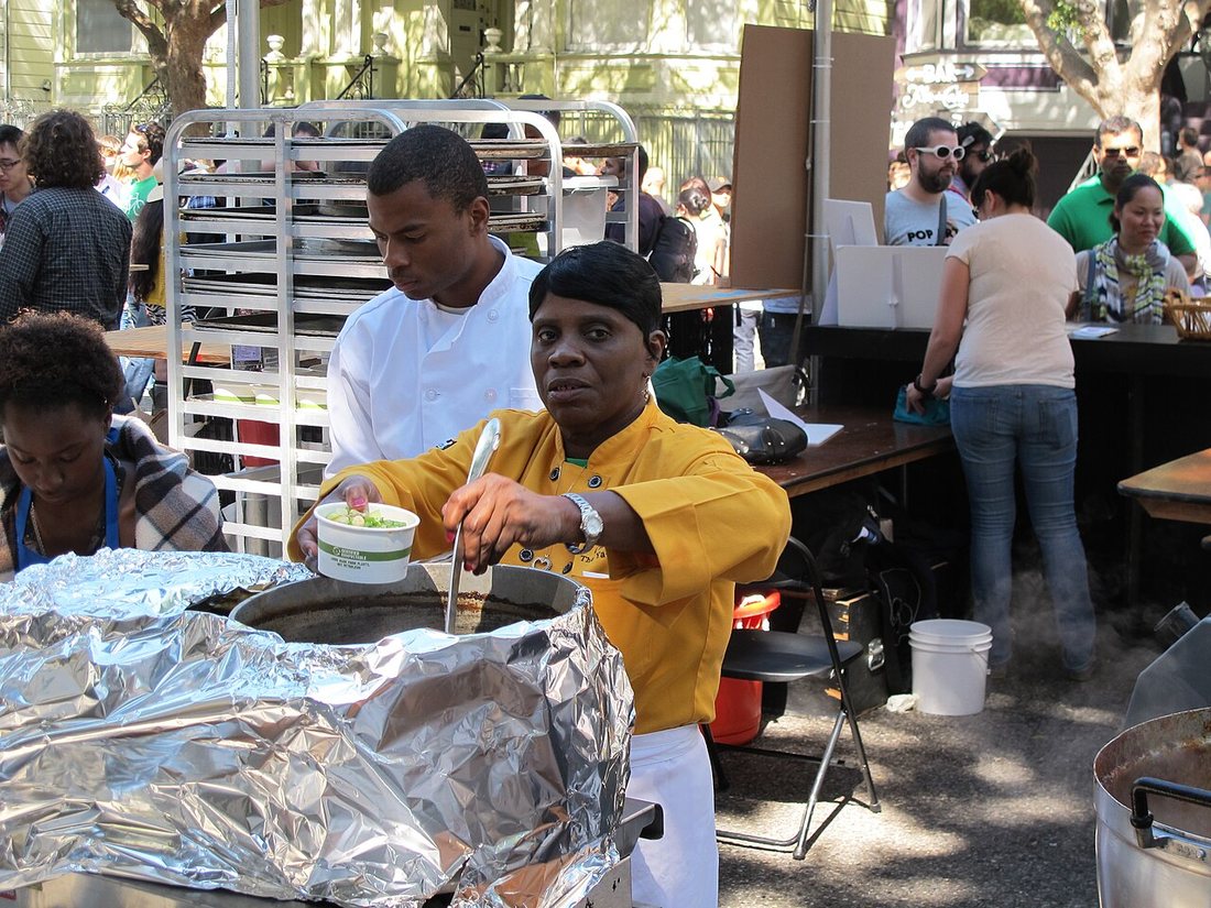 Linda Green in a yellow chef's jacket ladling soup from a foil-covered pot at a street food festival