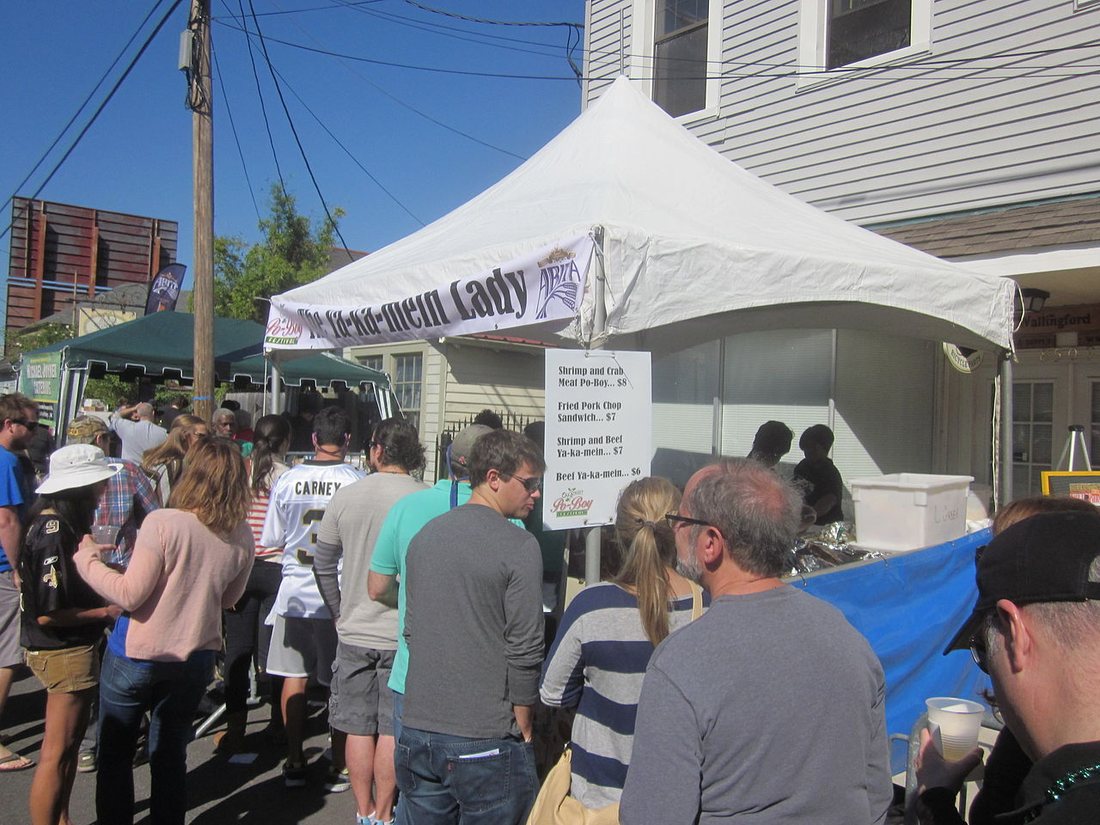 A line of customers at a white festival tent with a Ya-Ka-Mein Lady banner